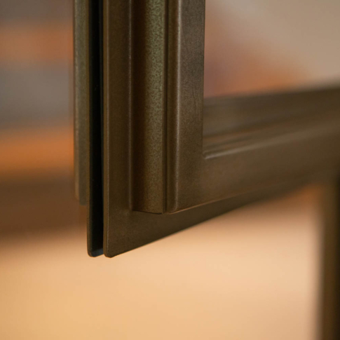 Detail van een bronzen stalen deur met verfijnde afwerking en slank profiel.